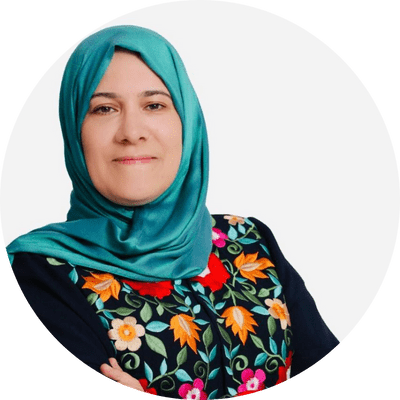 An arab woman wearing embroidered abaya and teal scarf, and smiling at the camera